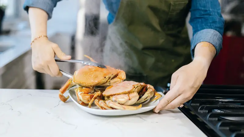 Crabes fraîchement cuits déposés à la pince sur une assiette blanche près d'une cuisinière
