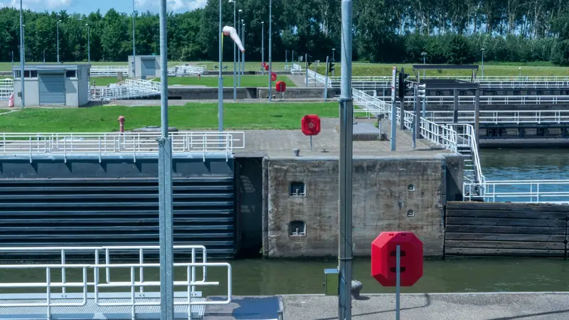Sas d'écluse en béton avec portes métalliques, garde-corps blancs et bouées de sauvetage rouges
