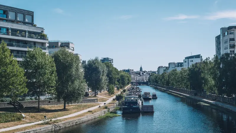 La Vilaine canalisée en ville, bordée d'arbres, de quais et d'immeubles, avec des bateaux amarrés le long de la berge