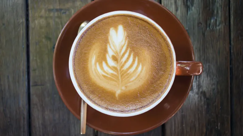 Tasse de café crème décorée d'une feuille de mousse de lait, posée sur une table en bois