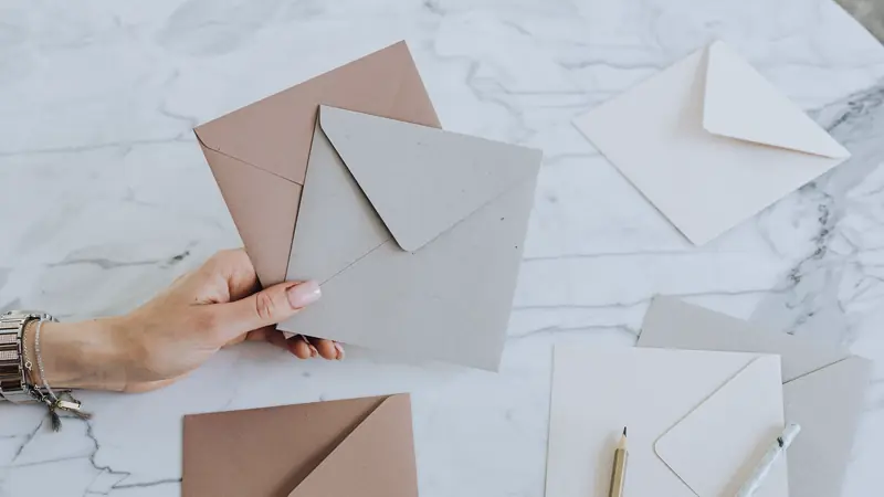 Main tenant des enveloppes de couleur au-dessus d'une table en marbre, avec cartes et crayons