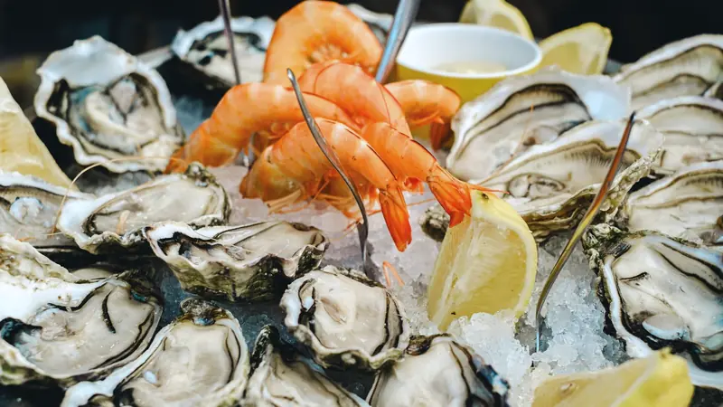 Plateau d'huîtres creuses ouvertes et de crevettes sur glace pilée, avec quartiers de citron
