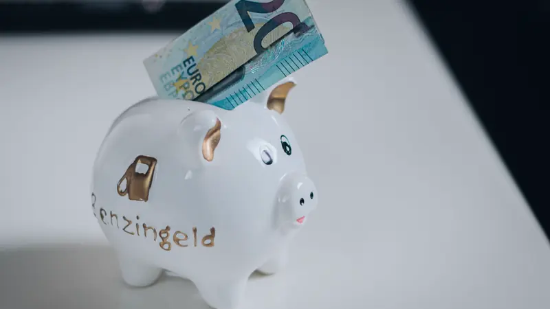 Tirelire en céramique blanche avec un billet de 20 euros glissé dans la fente