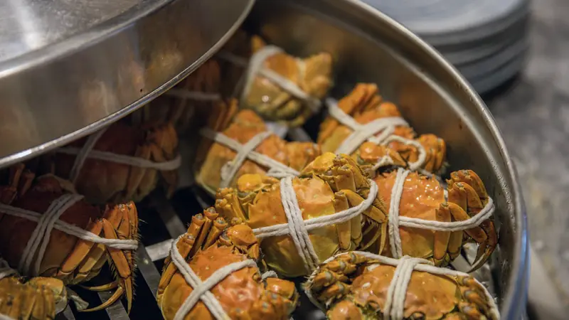 Crabes ficelés en cours de cuisson dans une marmite en inox entrouverte
