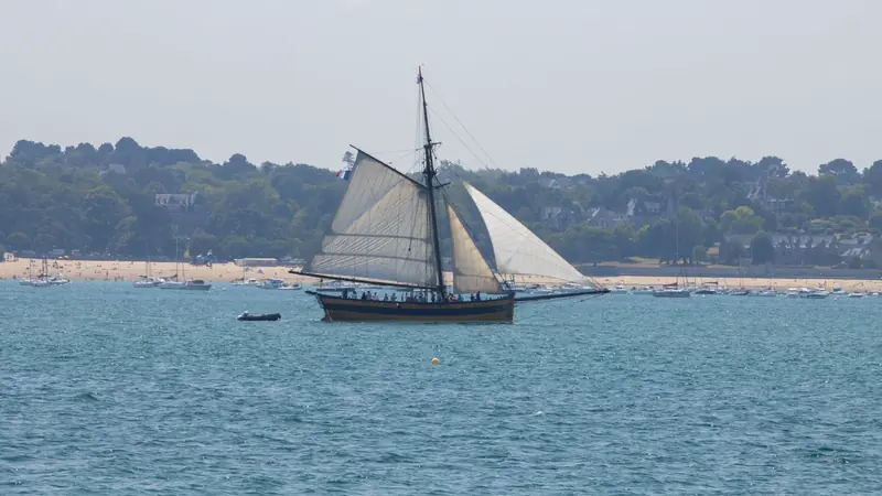 Voilier traditionnel à coque noire et jaune toutes voiles dehors dans une baie bordée de plages et de villas