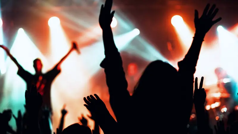 Silhouettes de spectateurs bras levés devant une scène de concert éclairée de projecteurs rouges et blancs