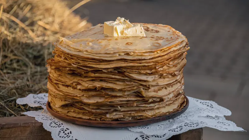 Haute pile de crêpes fines surmontée d'un morceau de beurre, sur un napperon