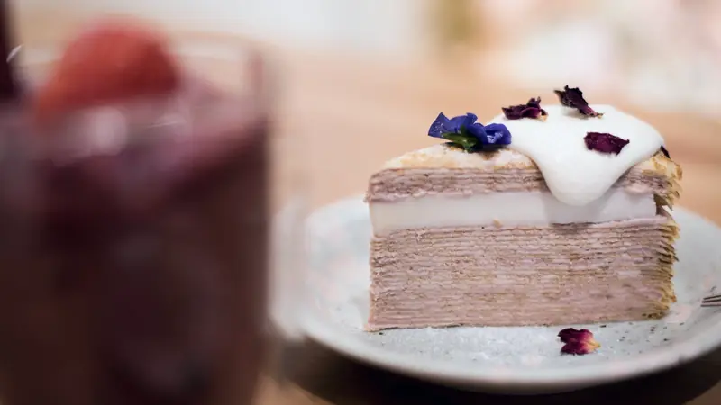Part de gâteau de crêpes aux couches roses et crème blanche, décorée de pétales