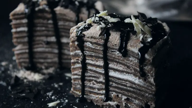 Parts de gâteau de crêpes au chocolat à étages, nappées de chocolat fondu et de copeaux