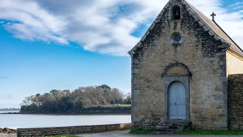 Petite chapelle de pierre au bord de l'eau sur l'île aux Moines, face à une rive boisée du golfe du Morbihan