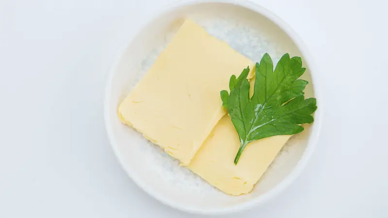 Deux plaquettes de beurre et une feuille de persil plat dans une coupelle blanche