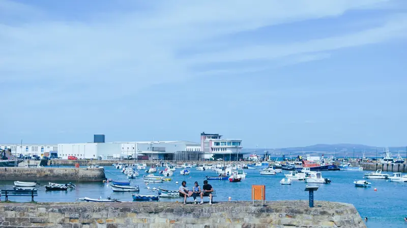Port breton abritant de nombreux petits bateaux derrière une digue de pierre, par beau temps