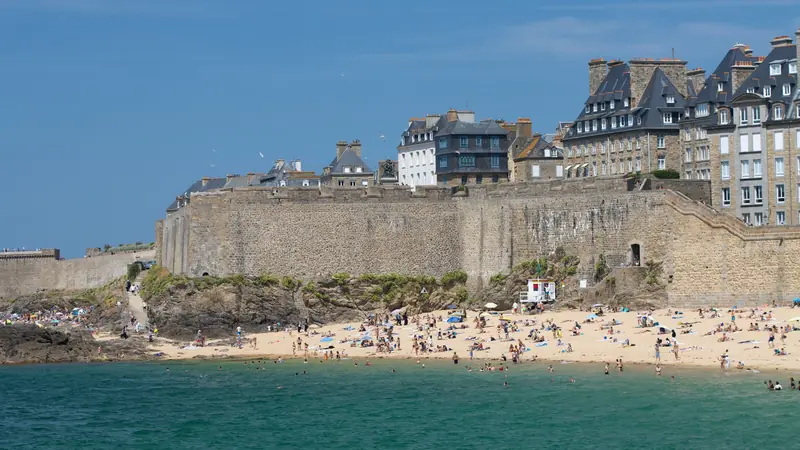 Remparts de Saint-Malo et immeubles de granit au-dessus d'une plage fréquentée, vus depuis la mer