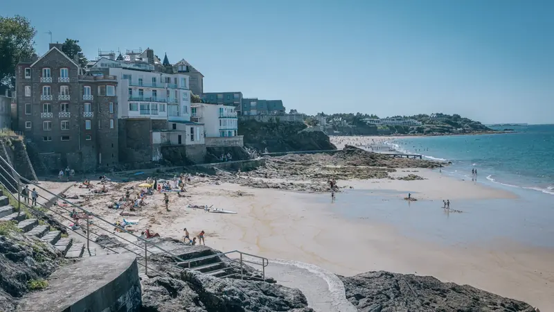 Immeubles et villas en pierre dominant une plage de sable et des rochers à marée basse à Dinard, sous un ciel d'été