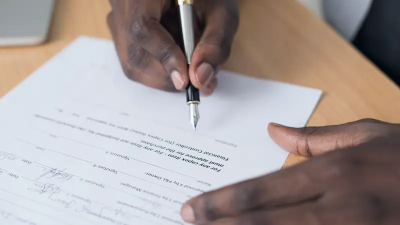 Mains qui signent un document au stylo plume sur un bureau en bois