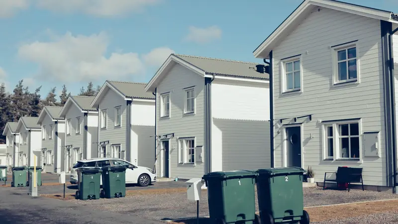 Rangée de maisons neuves à bardage clair dans un lotissement, avec leurs bacs à déchets devant