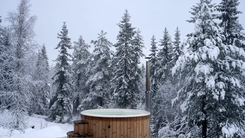 Bain nordique en bois chauffé au poêle, fumant au milieu d'une forêt de sapins enneigée