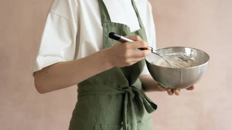 Pâte fouettée dans un saladier en inox tenu par une personne en tablier vert