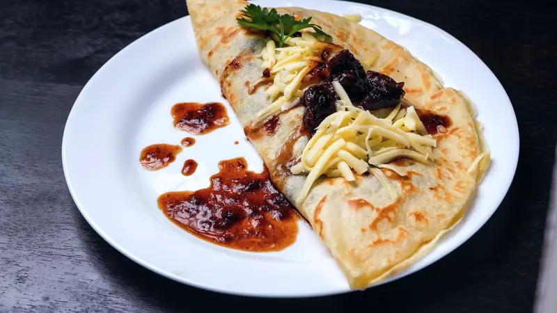 Crêpe dorée pliée, garnie de fromage râpé et de confiture, sur une assiette blanche
