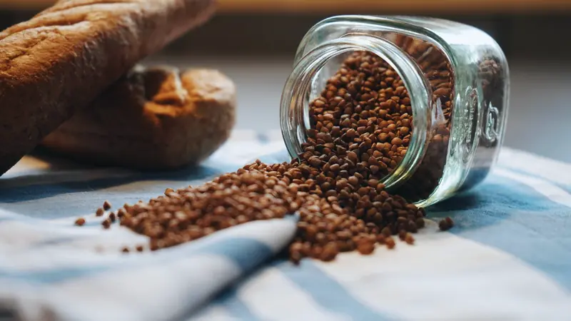 Grains de sarrasin s'échappant d'un bocal en verre renversé sur un torchon rayé