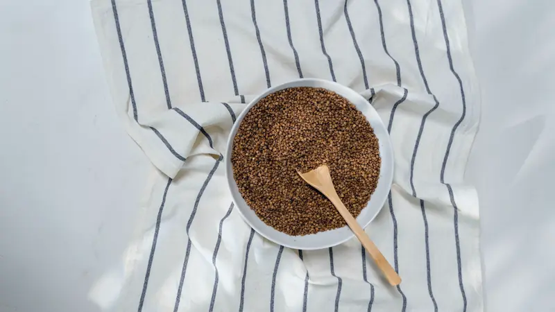 Bol en céramique rempli de grains de sarrasin crus, posé sur un tissu rayé