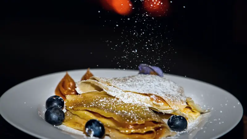 Crêpes pliées saupoudrées de sucre glace, avec caramel et myrtilles sur une assiette