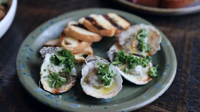 Trois huîtres chaudes gratinées au beurre et au persil, servies avec des tranches de pain grillé
