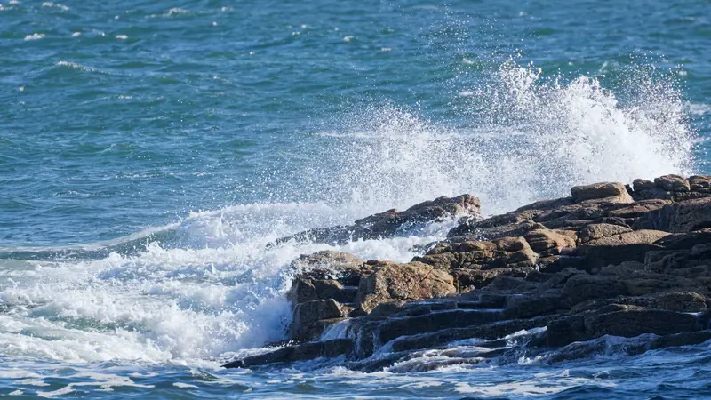 Vague qui se brise en gerbe d'écume contre des rochers de granit sur une mer agitée