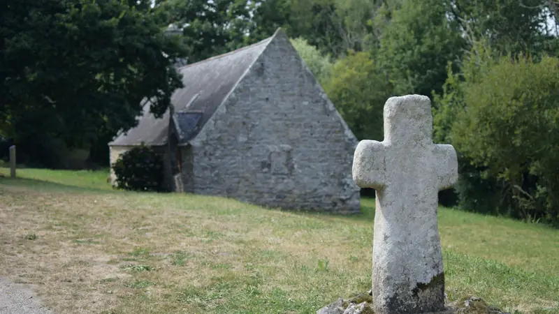 Croix de granite moussue devant une petite chapelle en pierre, dans la campagne bretonne