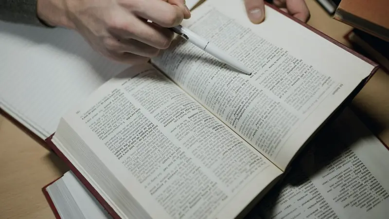 Main tenant un stylo au-dessus d'un dictionnaire ouvert sur une table