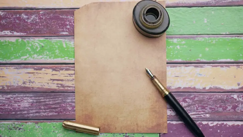 Feuille de papier vierge, encrier et stylo plume posés sur des planches peintes