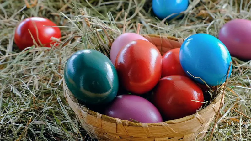 Œufs de Pâques peints en rouge, bleu, vert et rose dans un panier en osier posé sur du foin