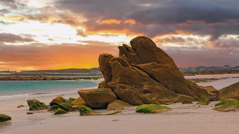 Gros rocher de granite sur une plage de sable clair au coucher du soleil, algues vertes sur les rochers