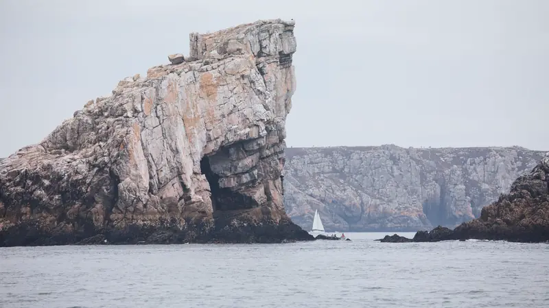 Rocher et hautes falaises de la presqu'île de Crozon, avec un voilier sur une mer calme sous un ciel gris